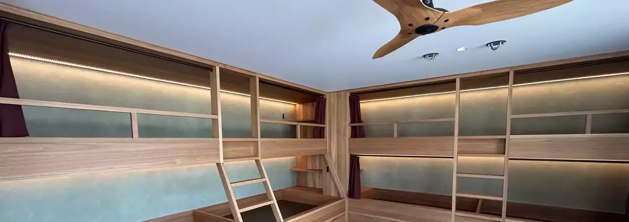 Built-in timber bunks with ladders and lit shelving lining two walls of a bunk room