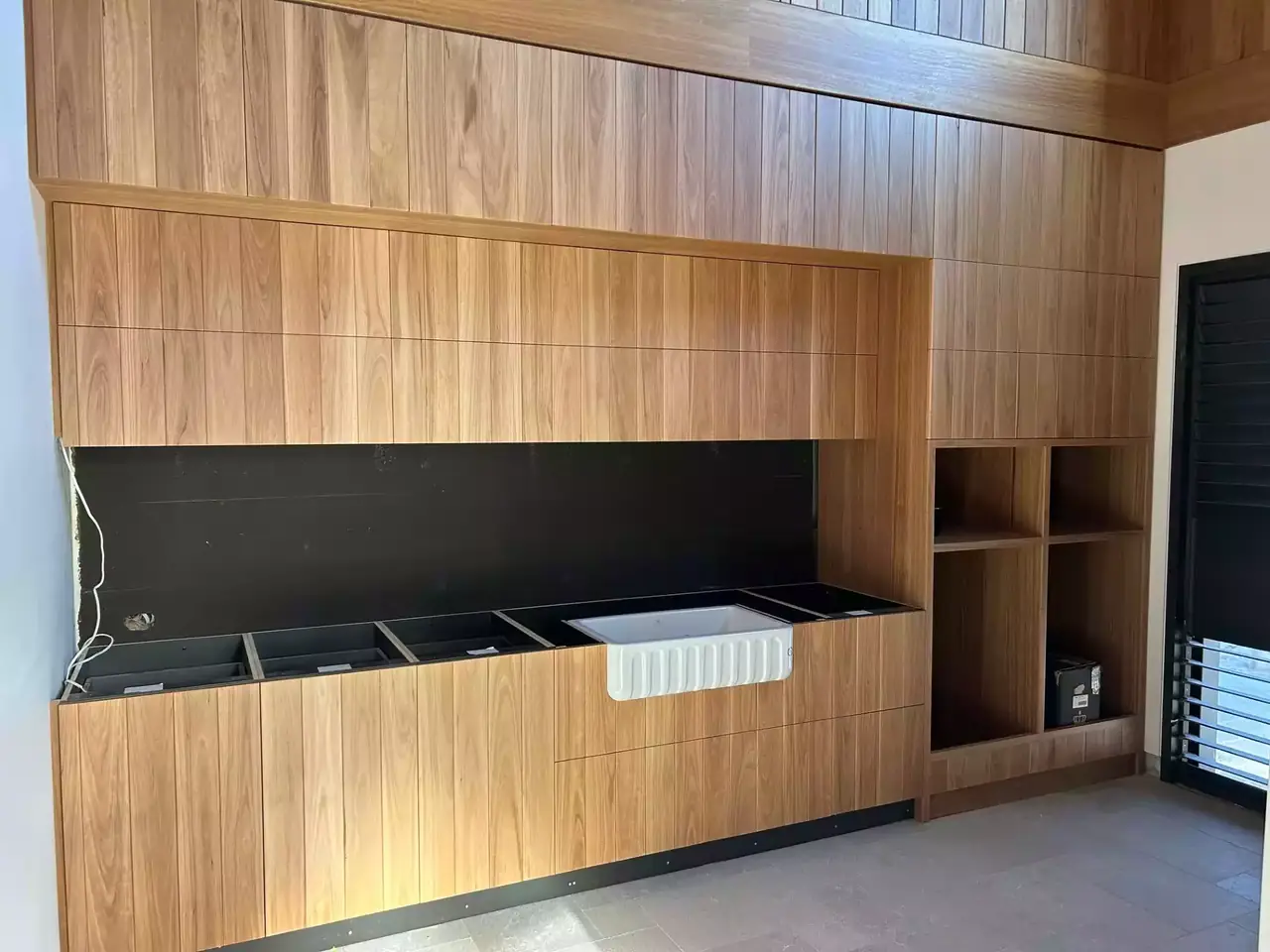 A wall of timber joinery mid-install, with the sink cut-outs still open and the benchtop in place