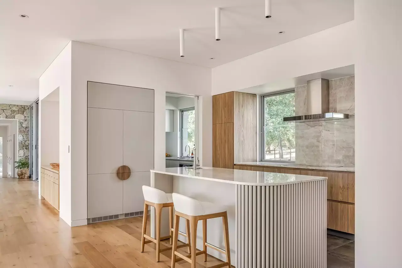 Open kitchen with a white fluted island, timber tall cabinetry and timber stools
