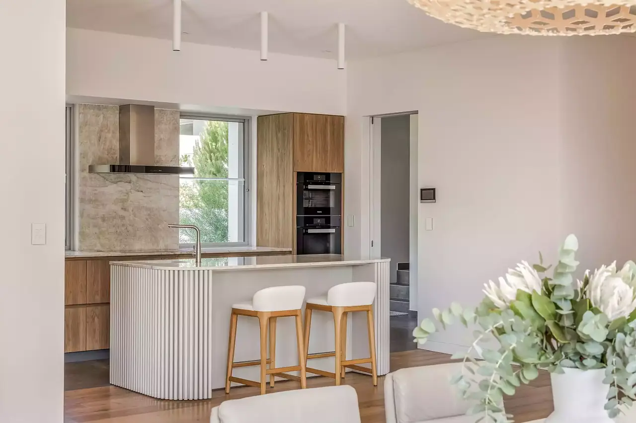 Fluted island end with timber stools and a stone splashback beyond