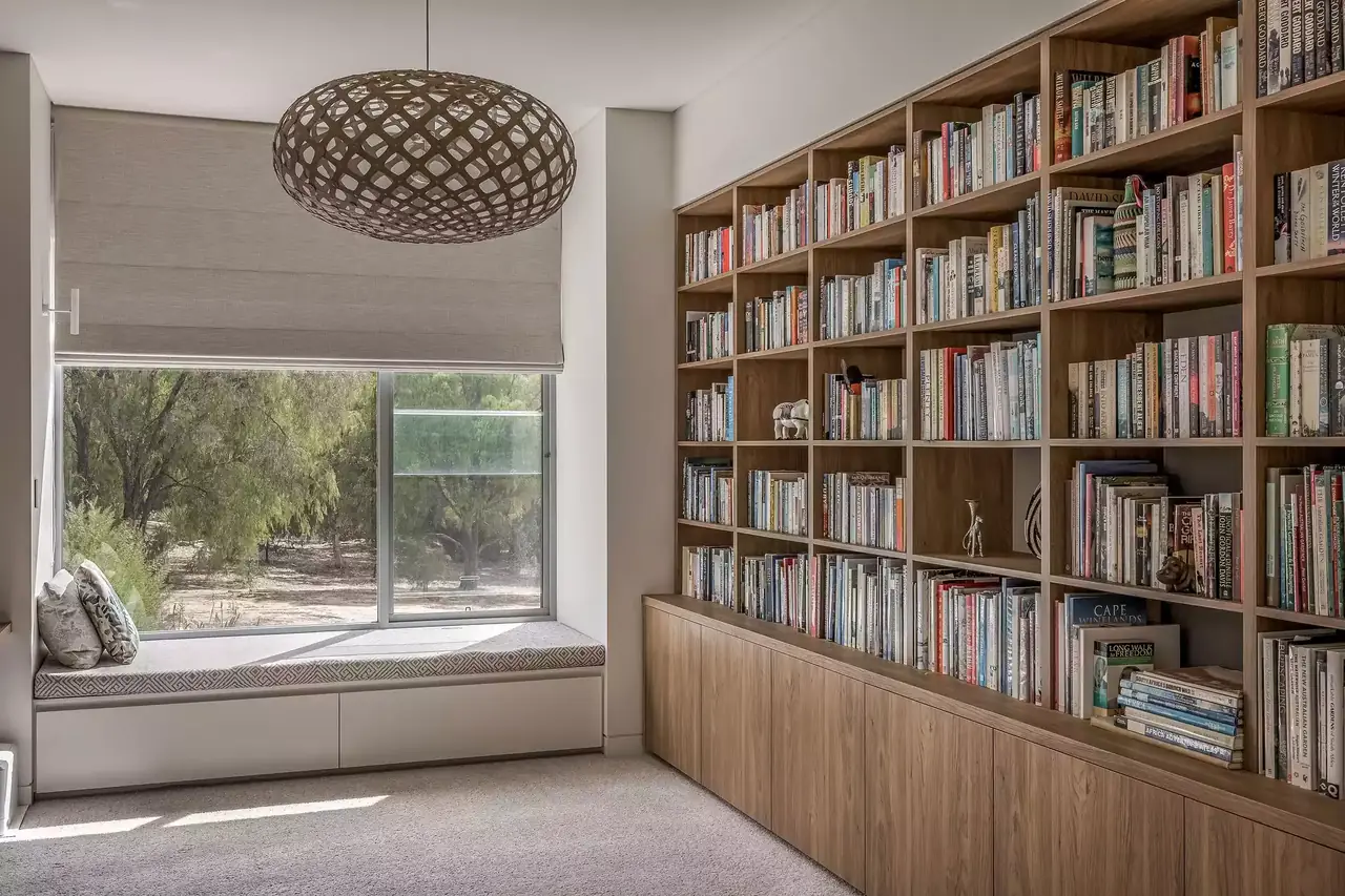 Study lined with built-in timber bookshelves beside an upholstered window seat