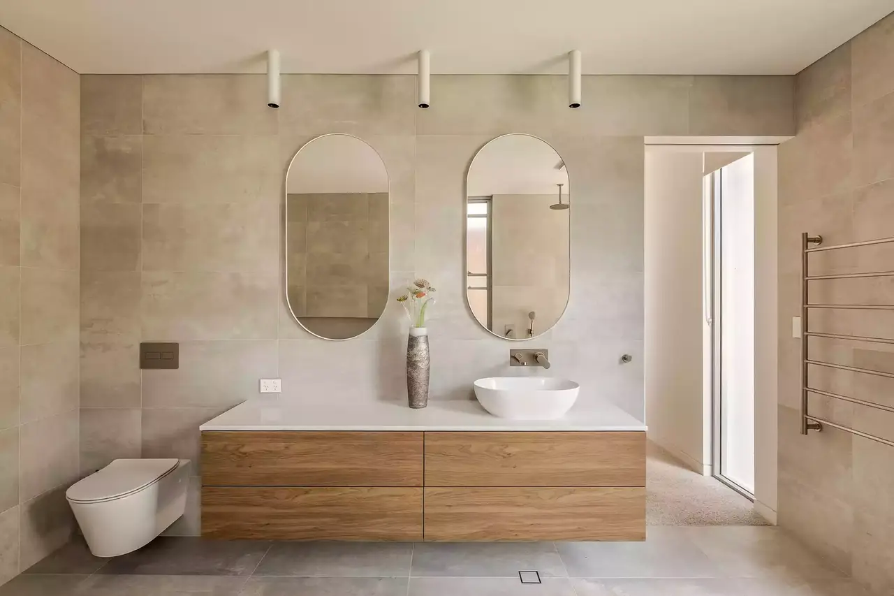 Floating timber vanity with a vessel basin beneath twin oval mirrors